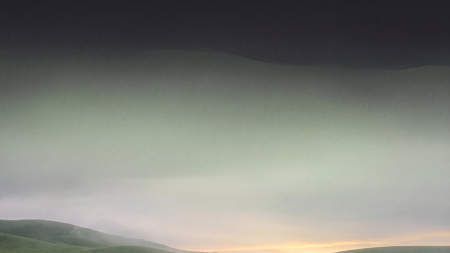 Il verde dell'Altopiano di Asiago, trattenuto nella nebbia, con una luce dorata all'orizzonte